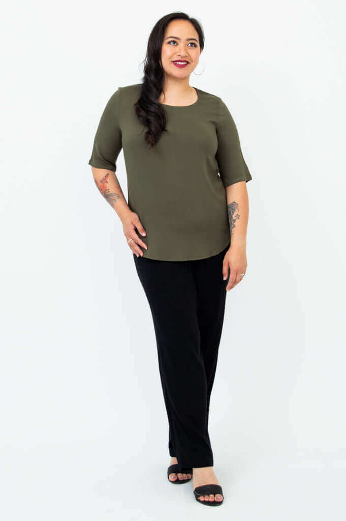 Woman posing in olive green blouse and black pants, angled view