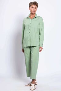Woman in light green shirt and pants, angled pose with hands by side