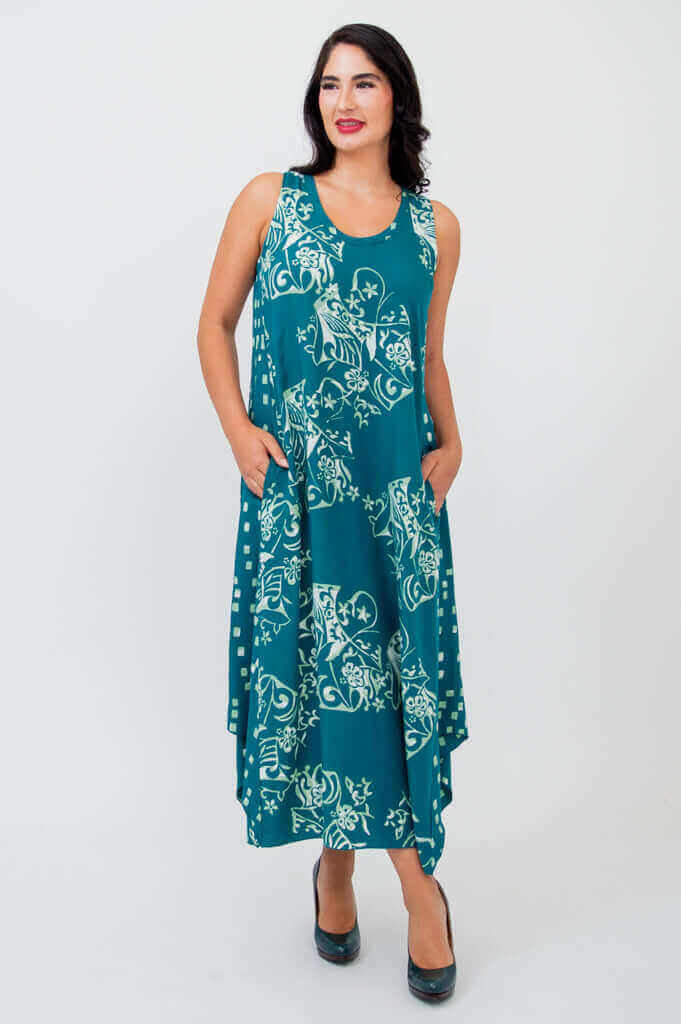 Model in sleeveless teal print midi dress standing with hands in pockets, angled right
