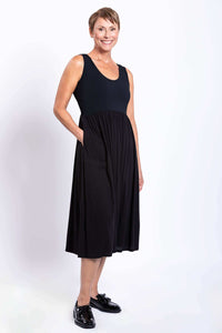 Angled side view of a woman in a black sleeveless empire waist midi dress, hand in pocket