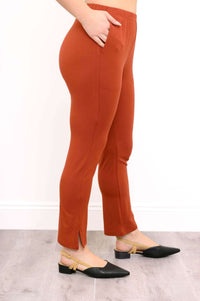 Angled side profile of a woman wearing rust copper bamboo pants with one hand resting in her side pocket.