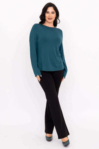 Three-quarter angled view of woman in teal Mona boat neck top and black pants