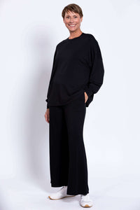 Model with hand in pocket, wearing relaxed black crew neck top and wide-leg pants