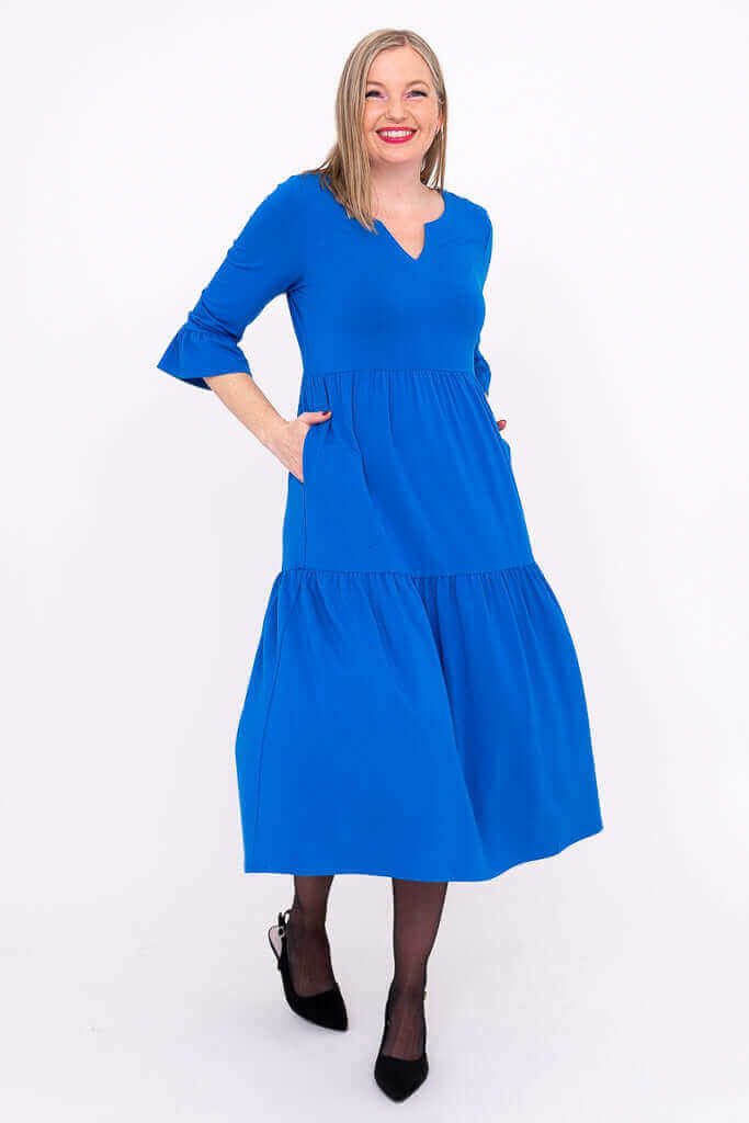 Angled view of a woman in a blue midi tiered dress with pockets and ruffle sleeves