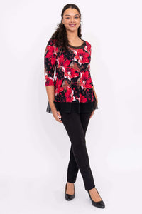 Woman posing in red floral top with mesh underlay and black pants, standing at an angle