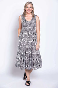 Front angle of a woman modeling a sleeveless black and white patterned dress with a scoop neck and pockets