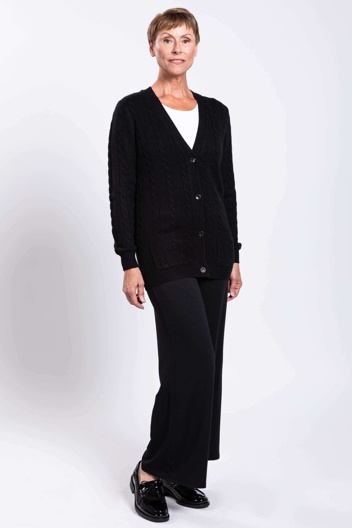 Angled view of a woman wearing a black cable knit cardigan with patch pockets
