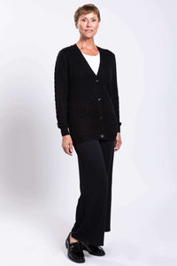 Angled view of a woman wearing a black cable knit cardigan with patch pockets