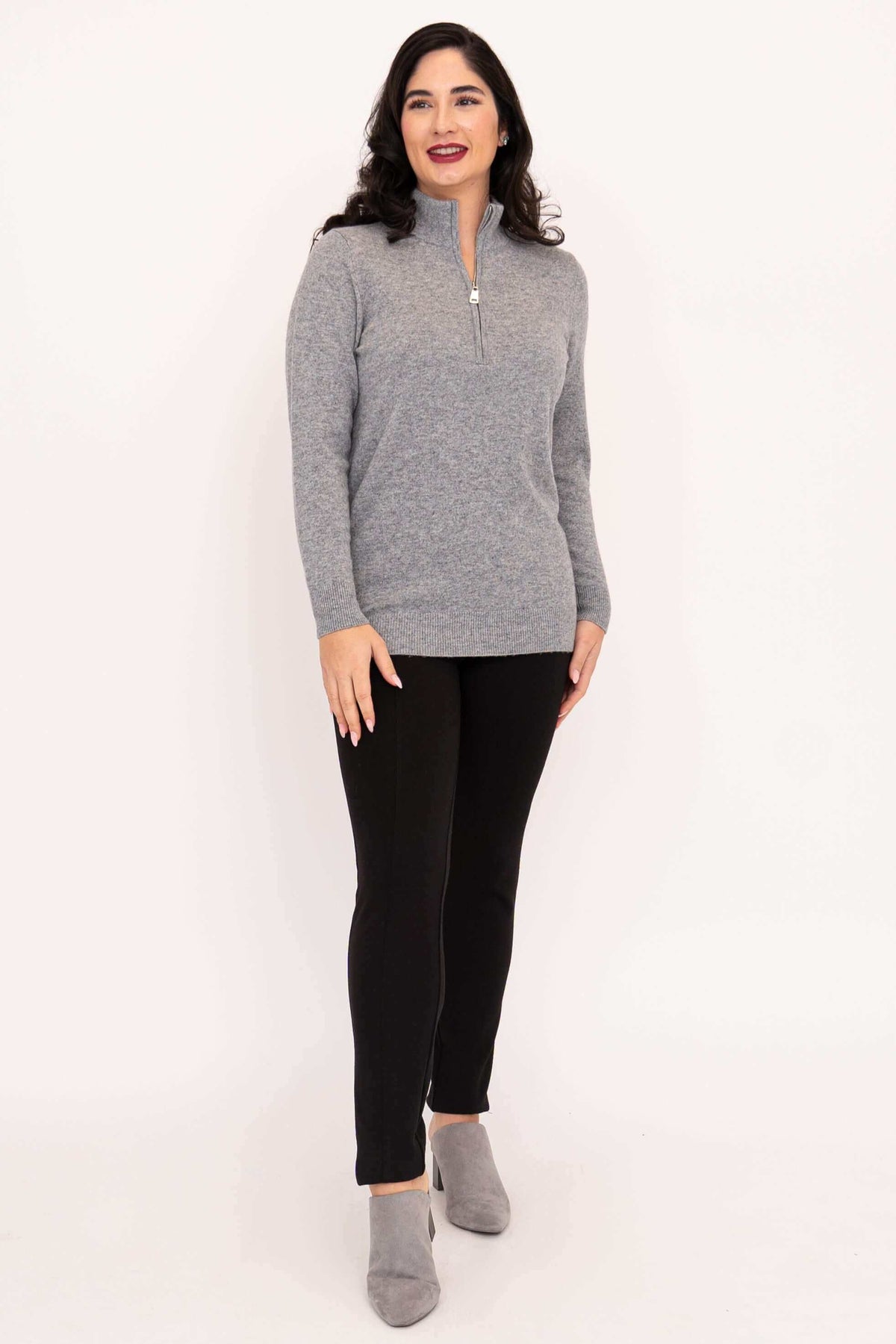 Woman standing in grey half zip sweater with black pants and grey shoes, angled view