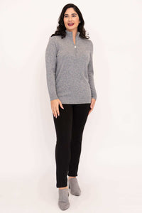 Woman standing in grey half zip sweater with black pants and grey shoes, angled view