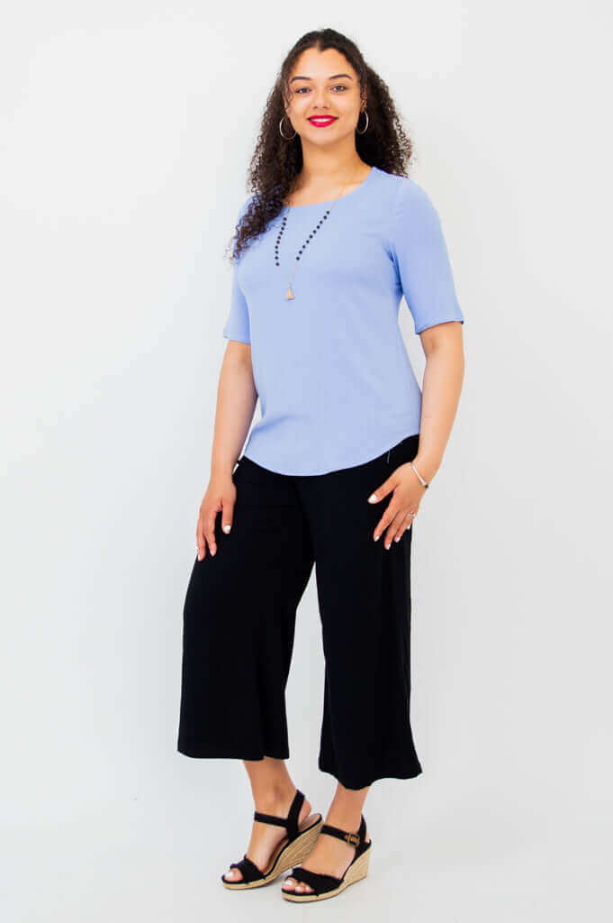 Full body angled view of model in light blue blouse and black pants