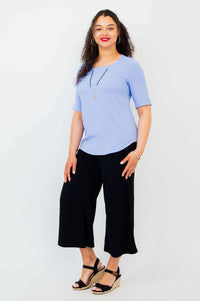 Full body angled view of model in light blue blouse and black pants