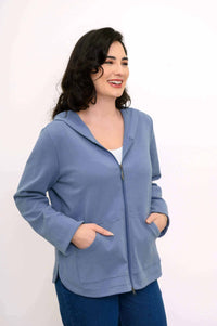 Woman in light blue hoodie jacket with hands in pockets, angled view