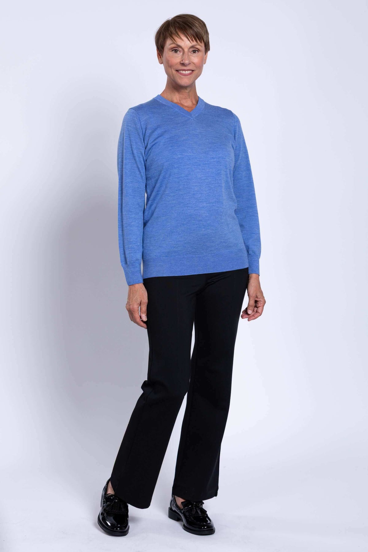 Woman in blue Merino V-neck sweater and black pants standing at an angle