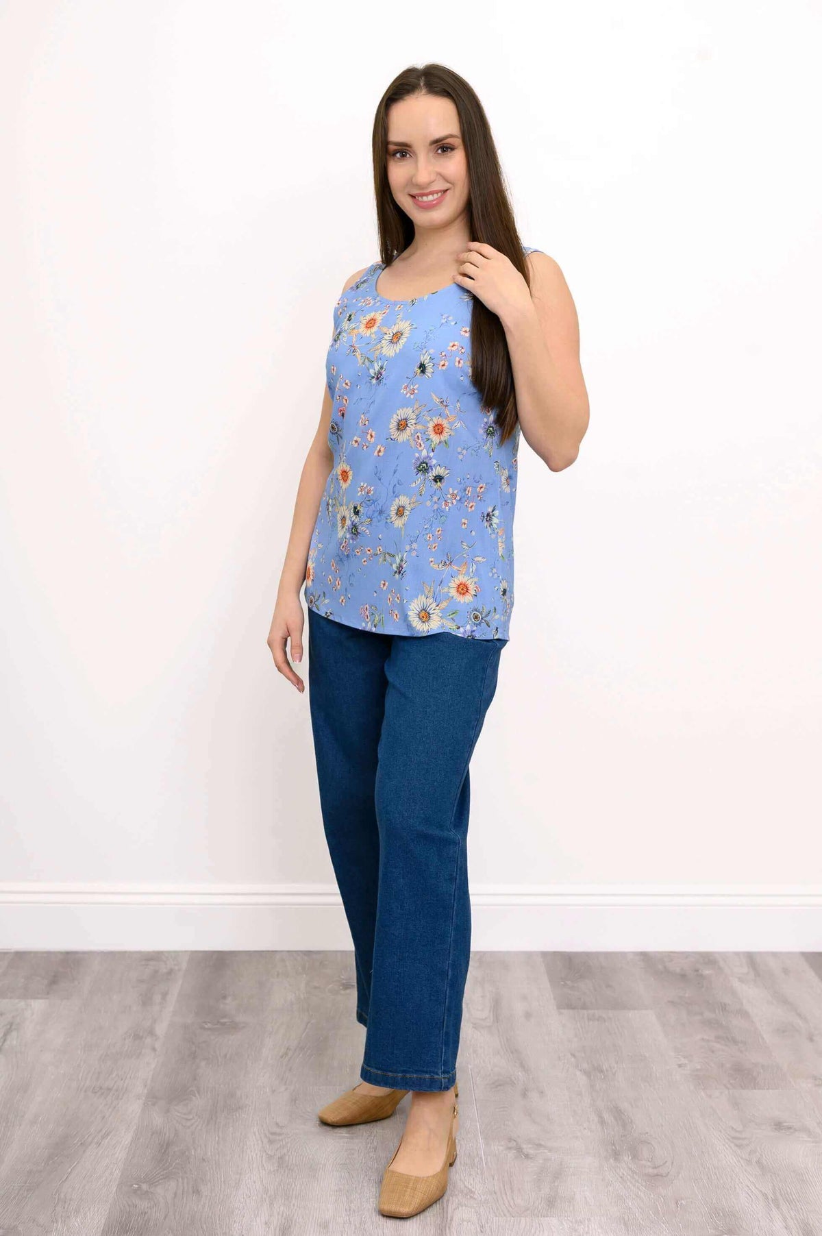 Woman standing in blue floral tank and blue jeans, smiling, angled view