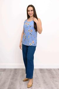 Woman standing in blue floral tank and blue jeans, smiling, angled view