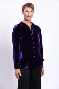 Woman in a deep purple velvet blouse, side-facing, hands down, smiling
