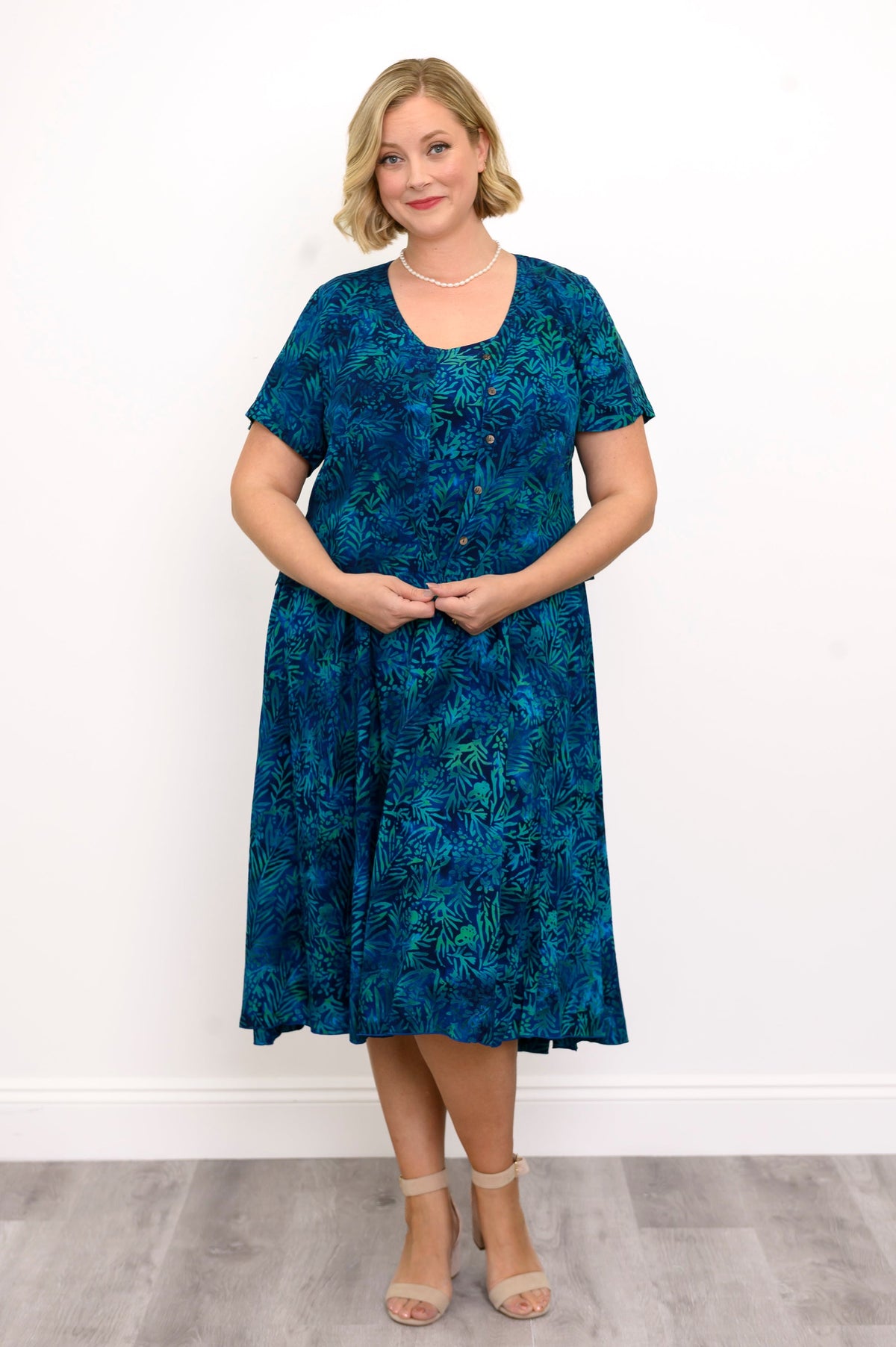 Woman wearing a blue patterned blouse and blue patterned dress against a white background, front view