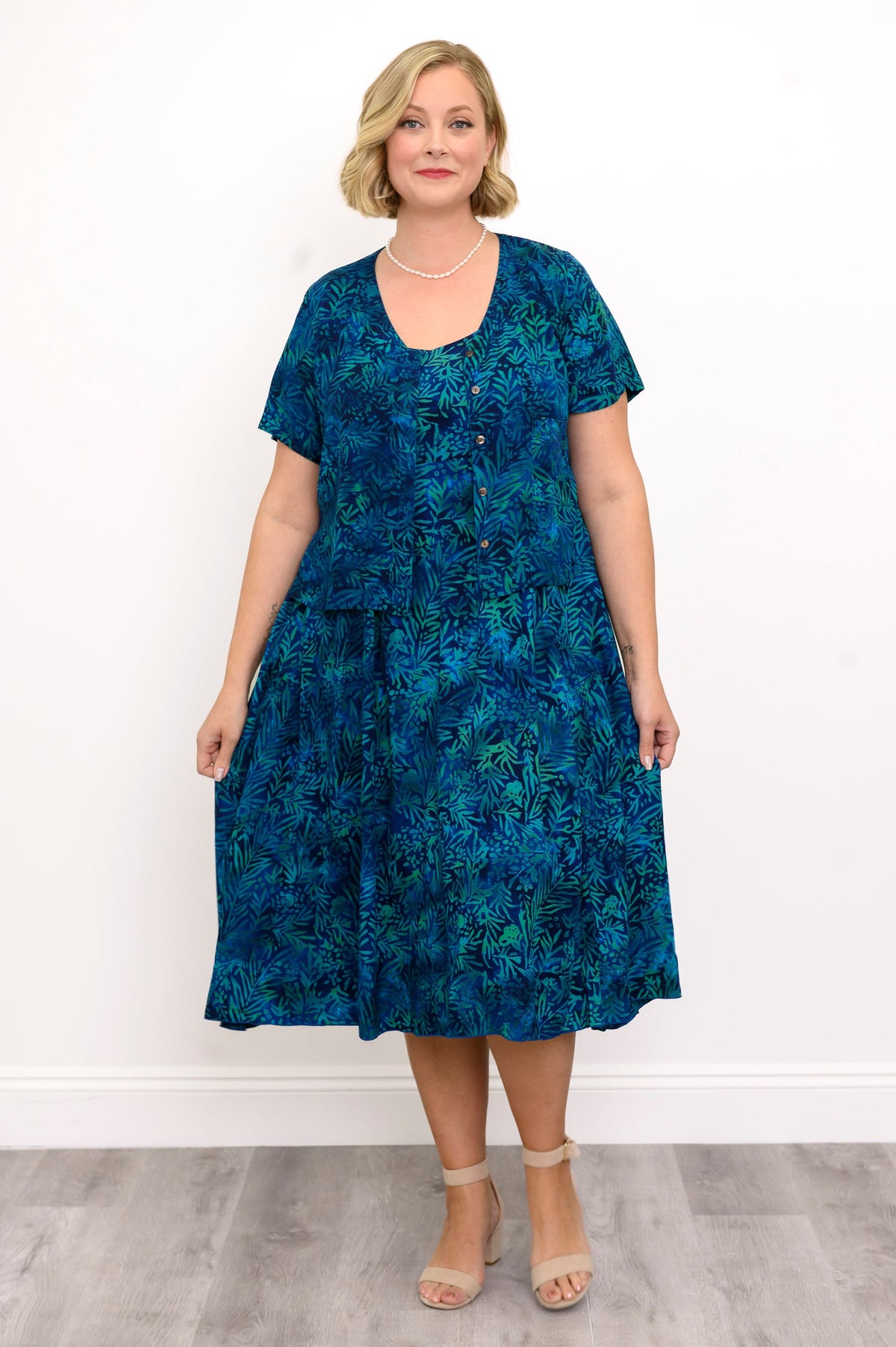 Woman wearing a blue patterned dress and blue patterned blouse against a white background, front view