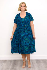 Woman wearing a blue patterned dress and blue patterned blouse against a white background, front view