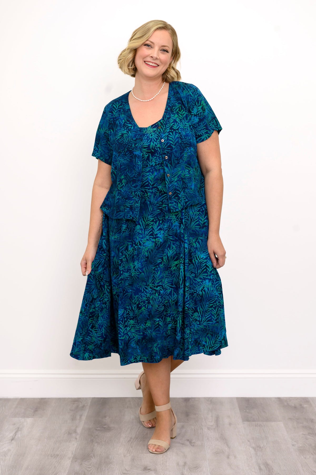 Woman wearing a blue patterned dress and blue patterned blouse against a white background, front view