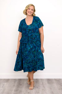 Woman wearing a blue patterned dress and blue patterned blouse against a white background, front view