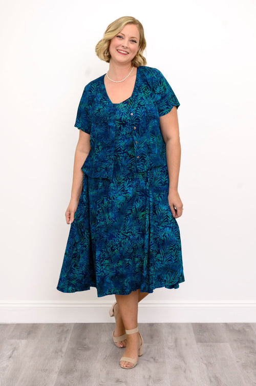 Woman wearing a blue patterned dress and blue patterned blouse against a white background, front view