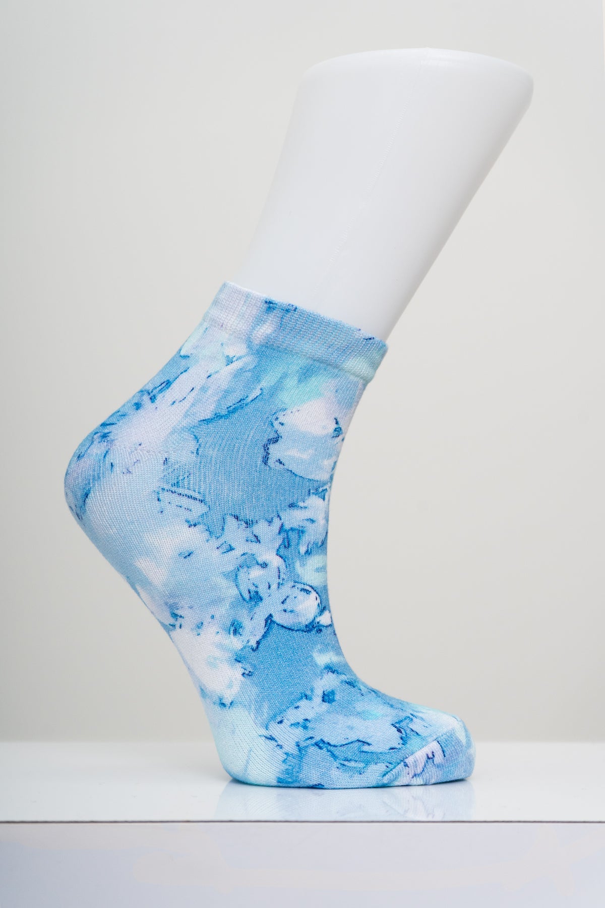 Blue and white tie dye cloud pattern ankle sock on a white display foot model against a gray studio backdrop.
