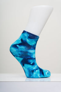 Vibrant blue and teal tie dye pattern ankle sock on a white display foot mannequin against a light gray background.
