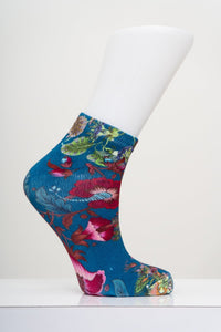 Teal tropical floral pattern ankle sock on a white display foot mannequin model against a light gray backdrop.