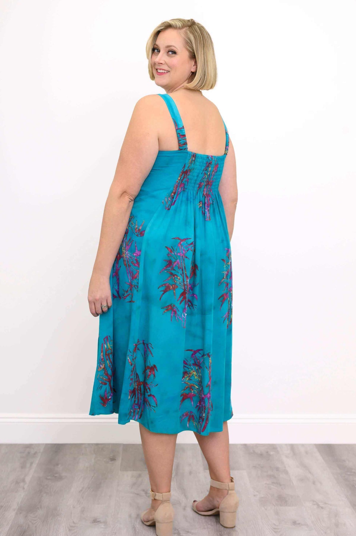 Back view of a woman in a sleeveless aqua blue midi dress with elasticized back