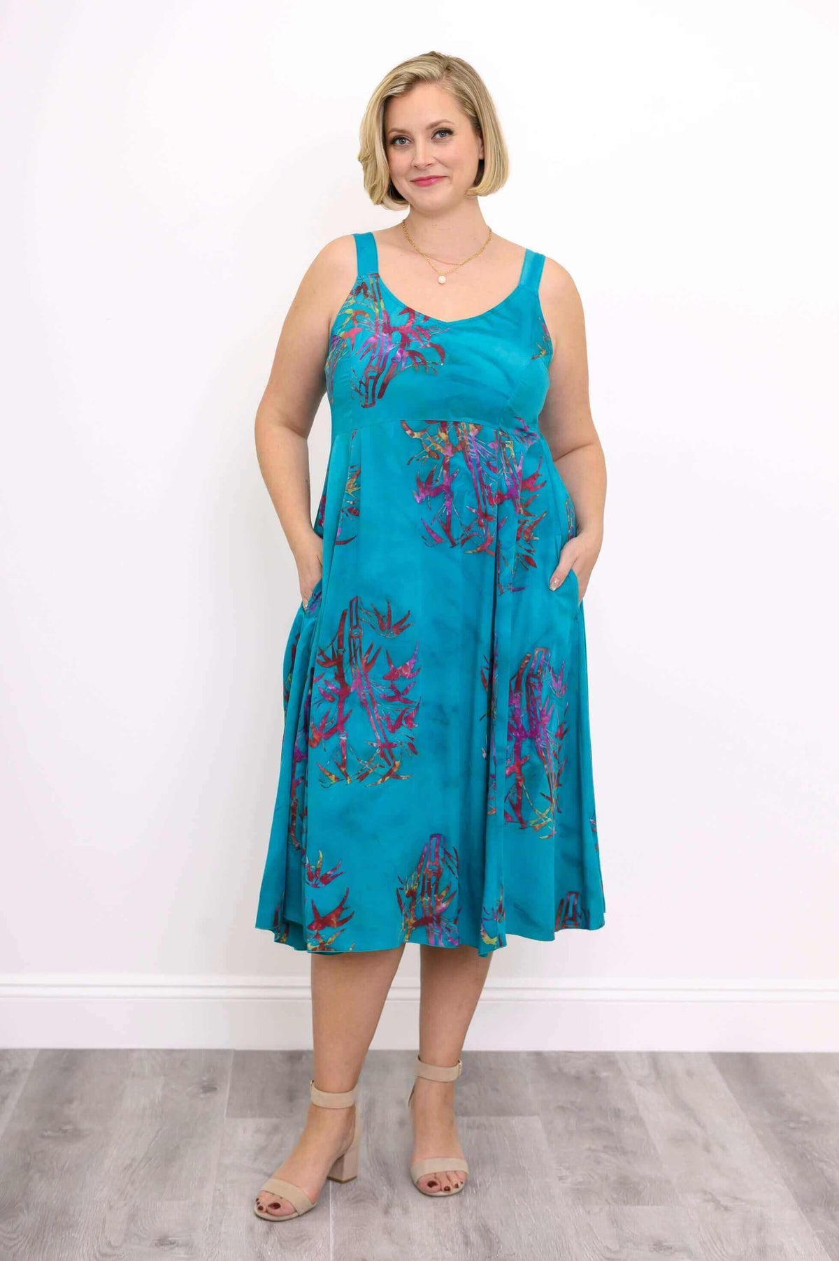 Woman showcasing pockets on an aqua blue midi dress with purple floral print