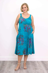 Woman showcasing pockets on an aqua blue midi dress with purple floral print