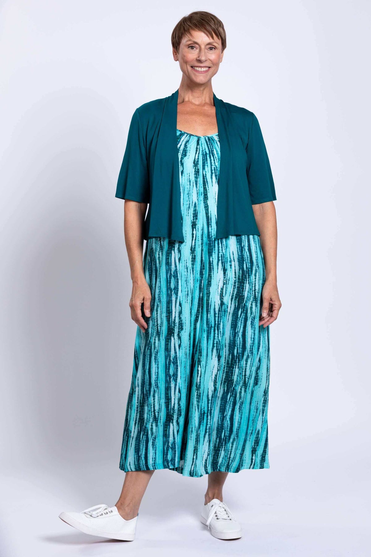 Full view of woman in aqua jumpsuit and teal cardigan, hands by side