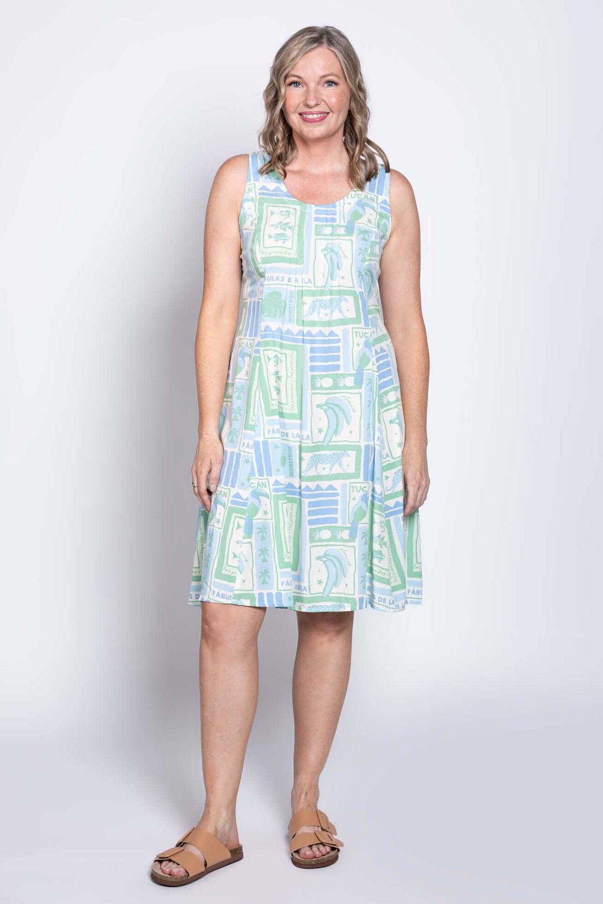 Woman wearing sleeveless Arden dress with tropical green and blue print, front view