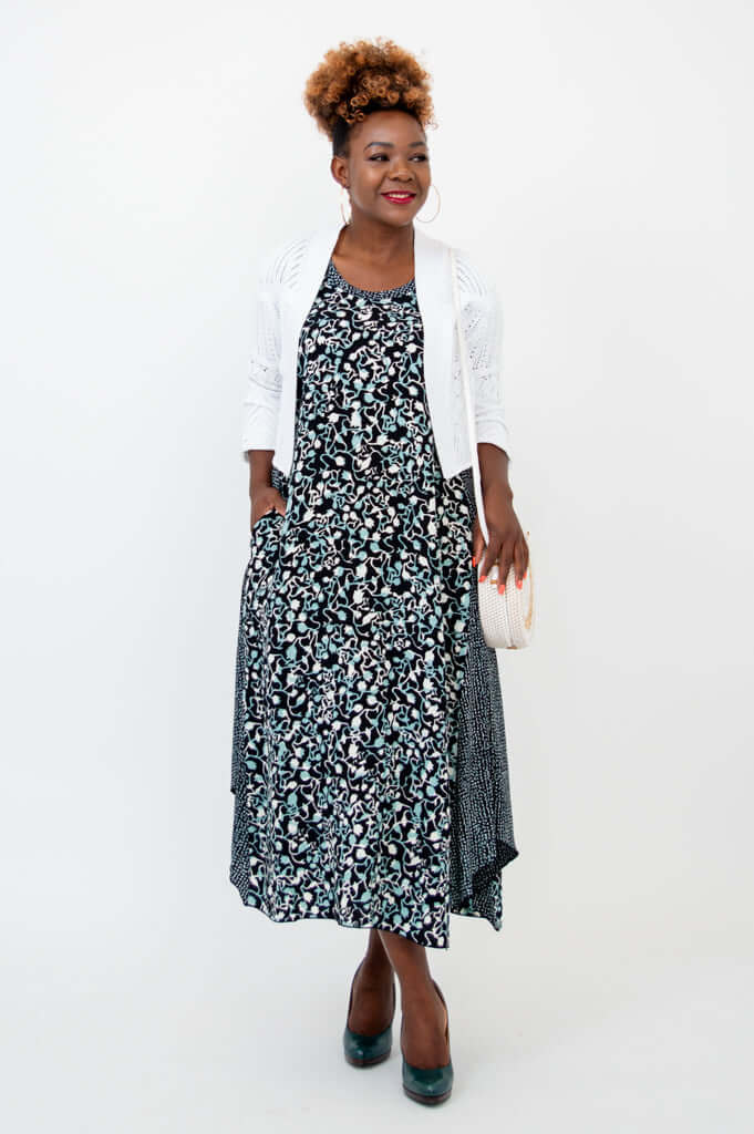 Model in black and blue tank dress with white cardigan and clutch bag