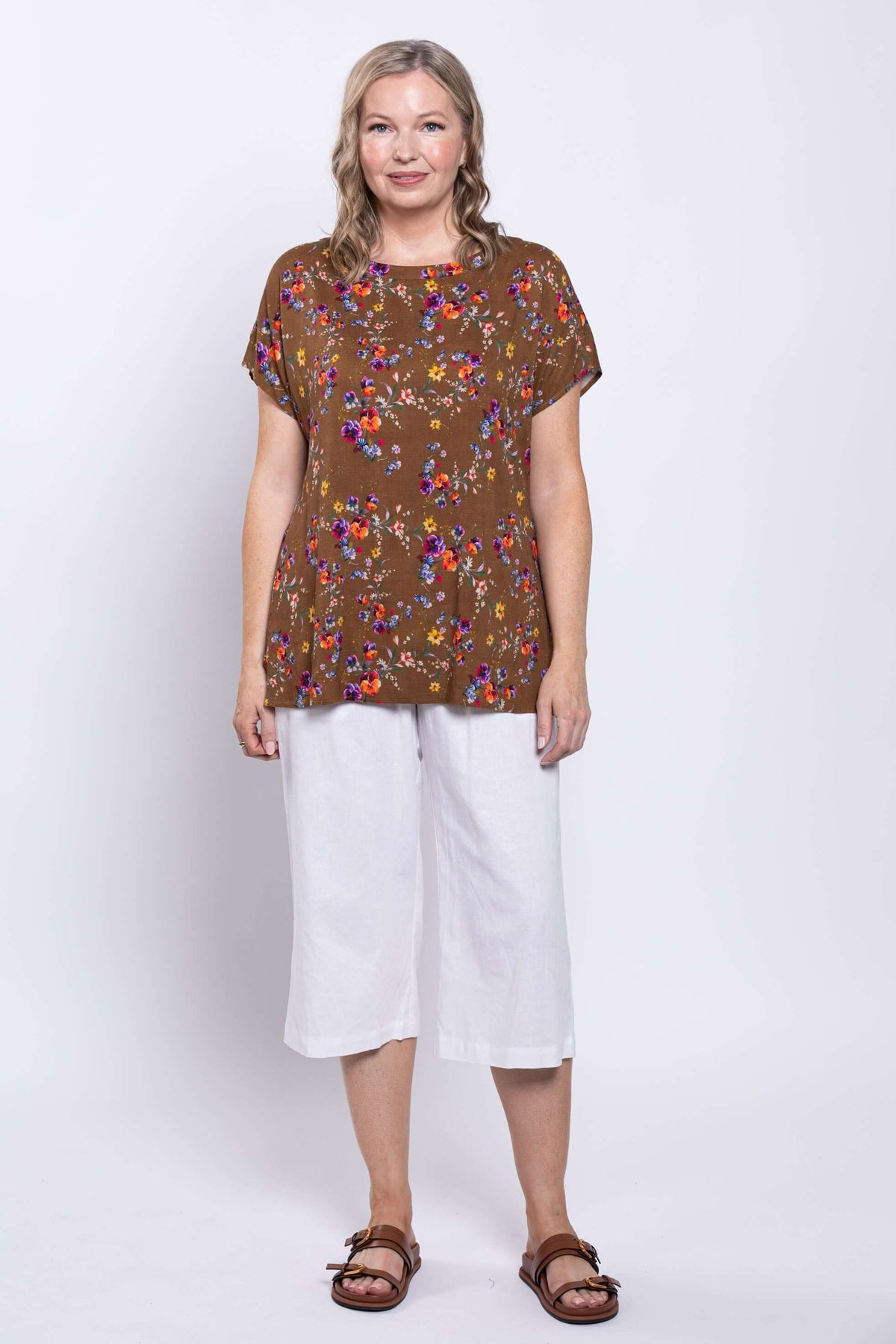 Model in brown top with multicolor floral print, styled with white culottes and brown sandals