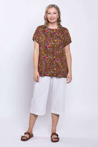 woman smiling and looking at the camera as she wears a flower print top and white capri pants