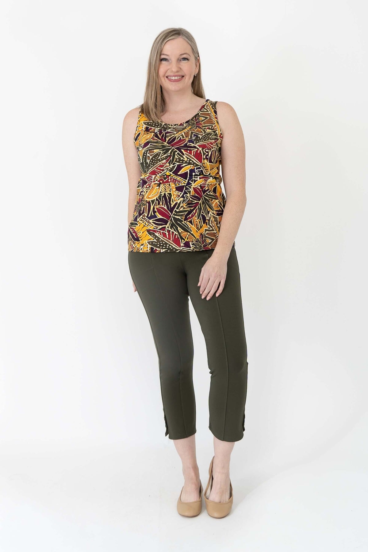 Woman smiling in sleeveless marigold batik tank top and green pants, frontal full-body view