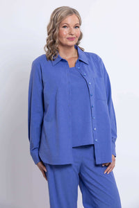 Woman in azure button-up shirt and matching pants, chest-up, smiling, front angle
