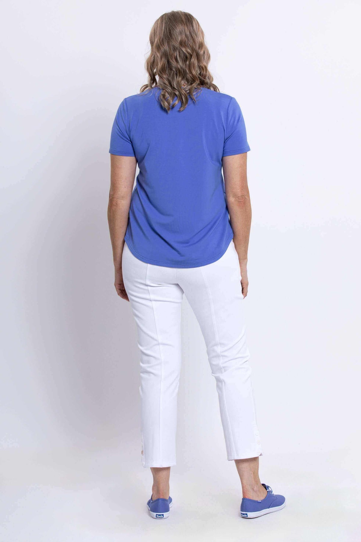 Back view of woman in azure blue bamboo tee and white pants, showing shirt hem
