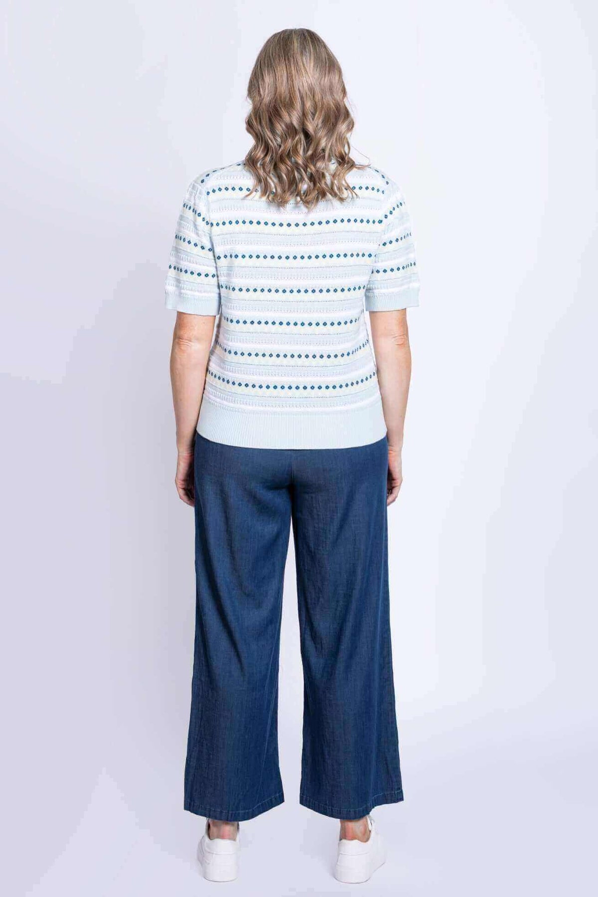 Back view of woman wearing a blue eyelet stripe short sleeve sweater and wide-leg pants