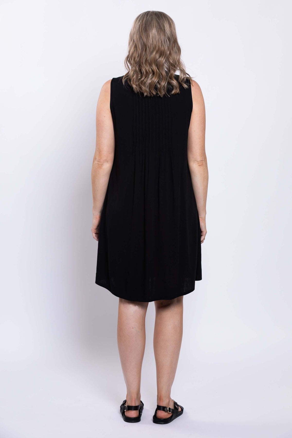 Back view of woman in a sleeveless black A-line dress showcasing pintucked rear panel