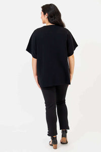 Back view of woman wearing a black cotton cardigan with relaxed fit and cropped sleeves