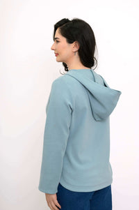 Back and side view of woman in a light blue hoodie showing the hood and relaxed fit
