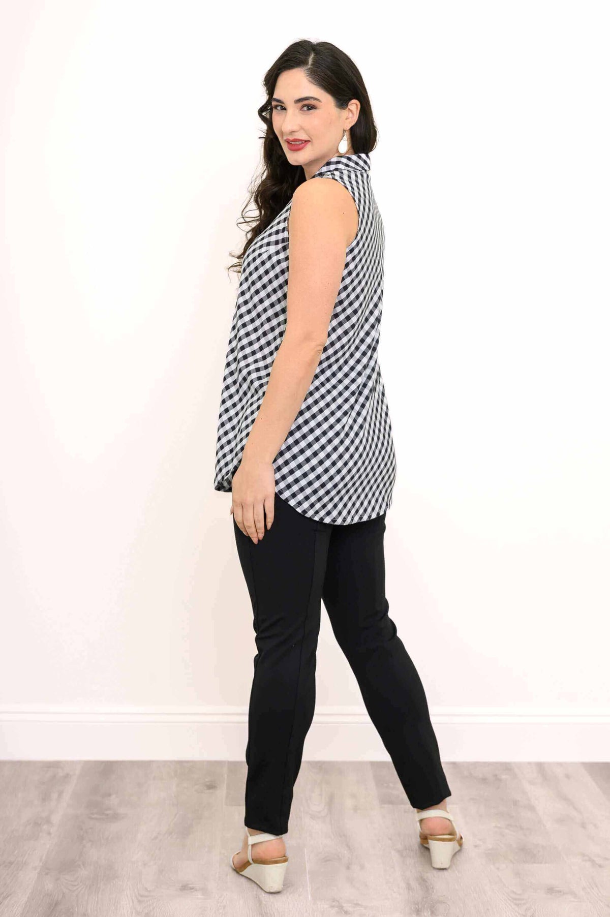 Back angled view of a woman in a gingham sleeveless tank top and black pants