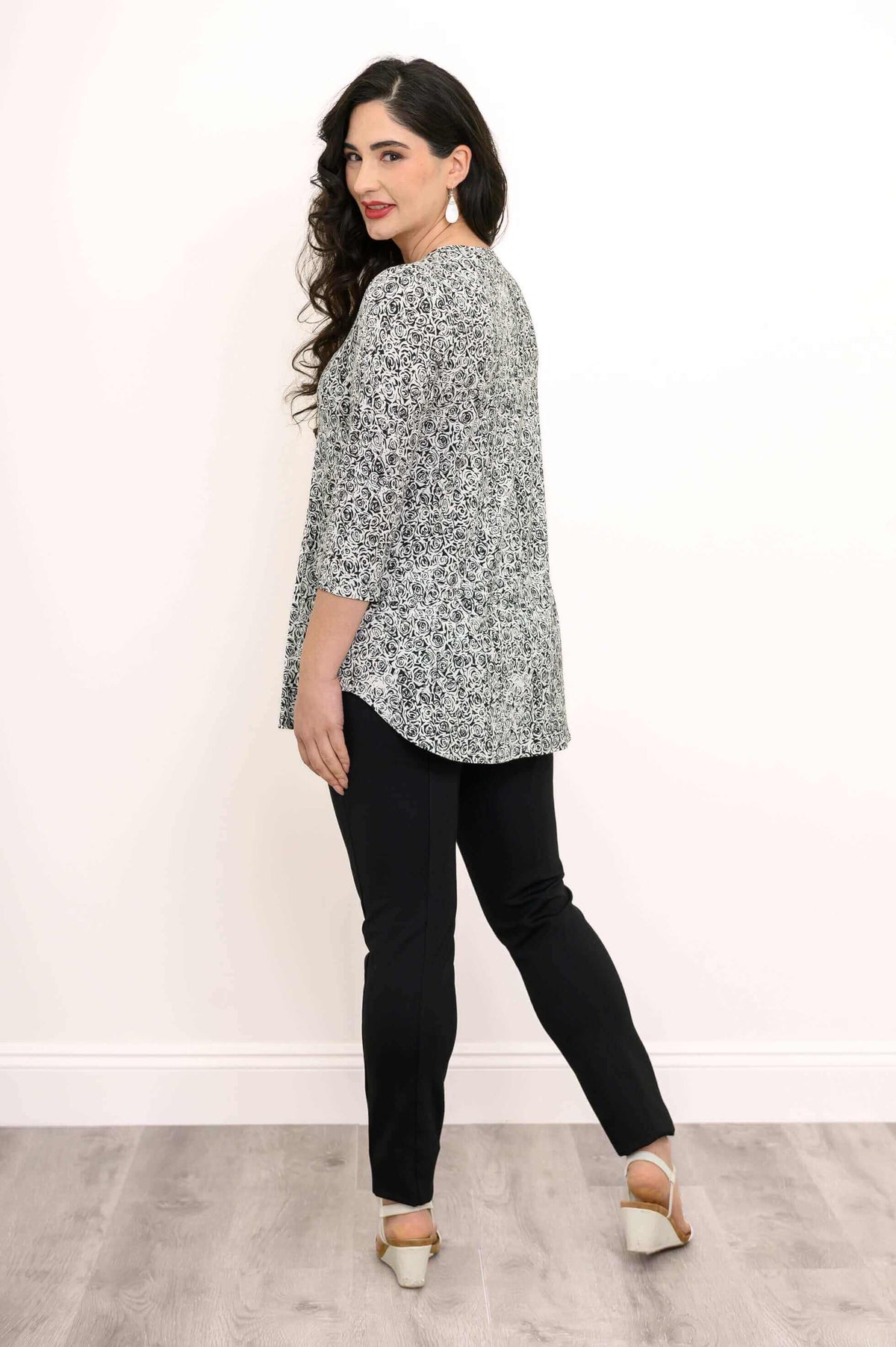 Back angle of woman modelling black and white floral top with rounded hem and black pants
