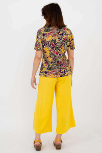 Back view of botanical print boatneck tee and yellow pants on woman