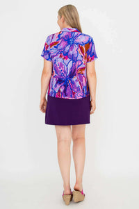 Back view of model in purple abstract floral collared blouse with purple skirt