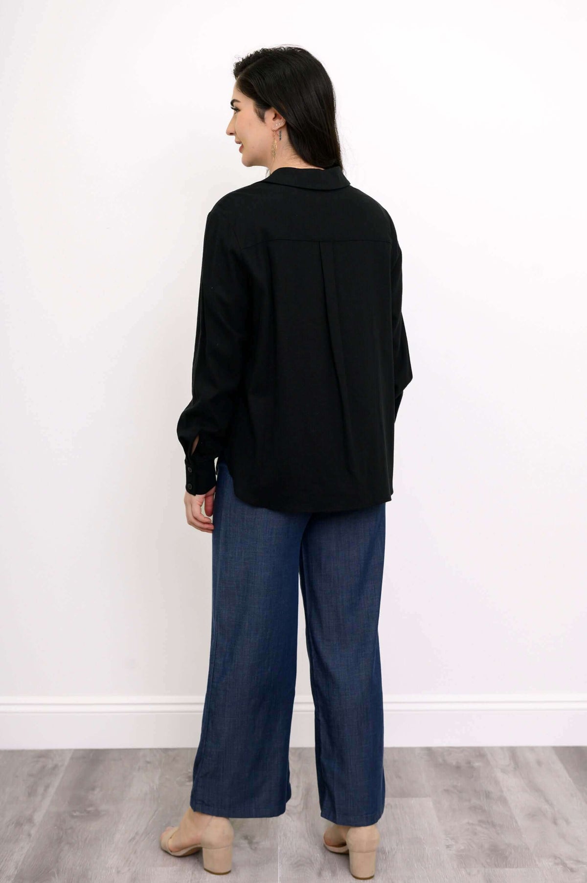 Back view of a woman wearing a black button-up shirt with center back pleat and blue jeans